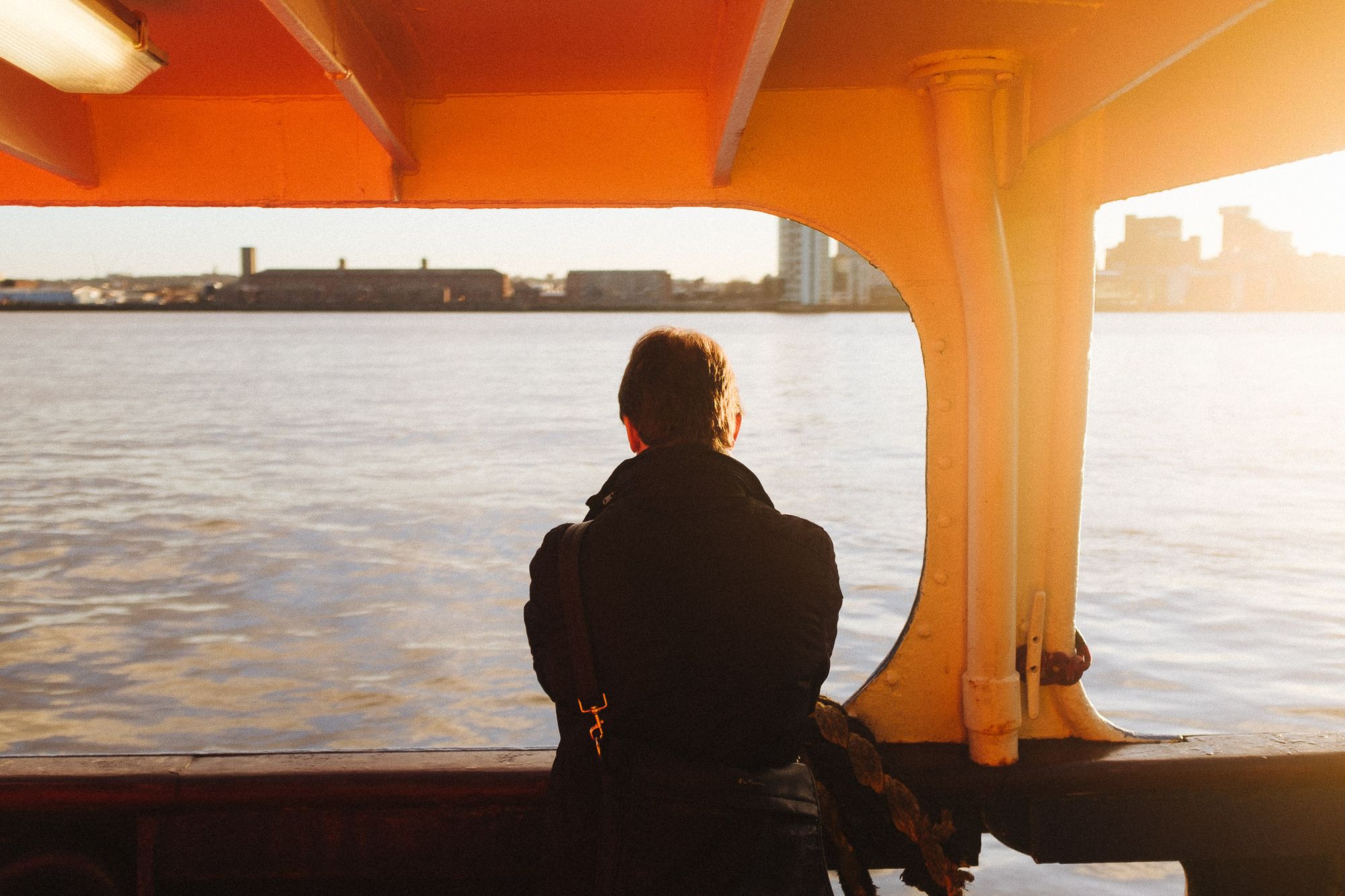 A person looks across the river as a ferry sails towards Liverpool.