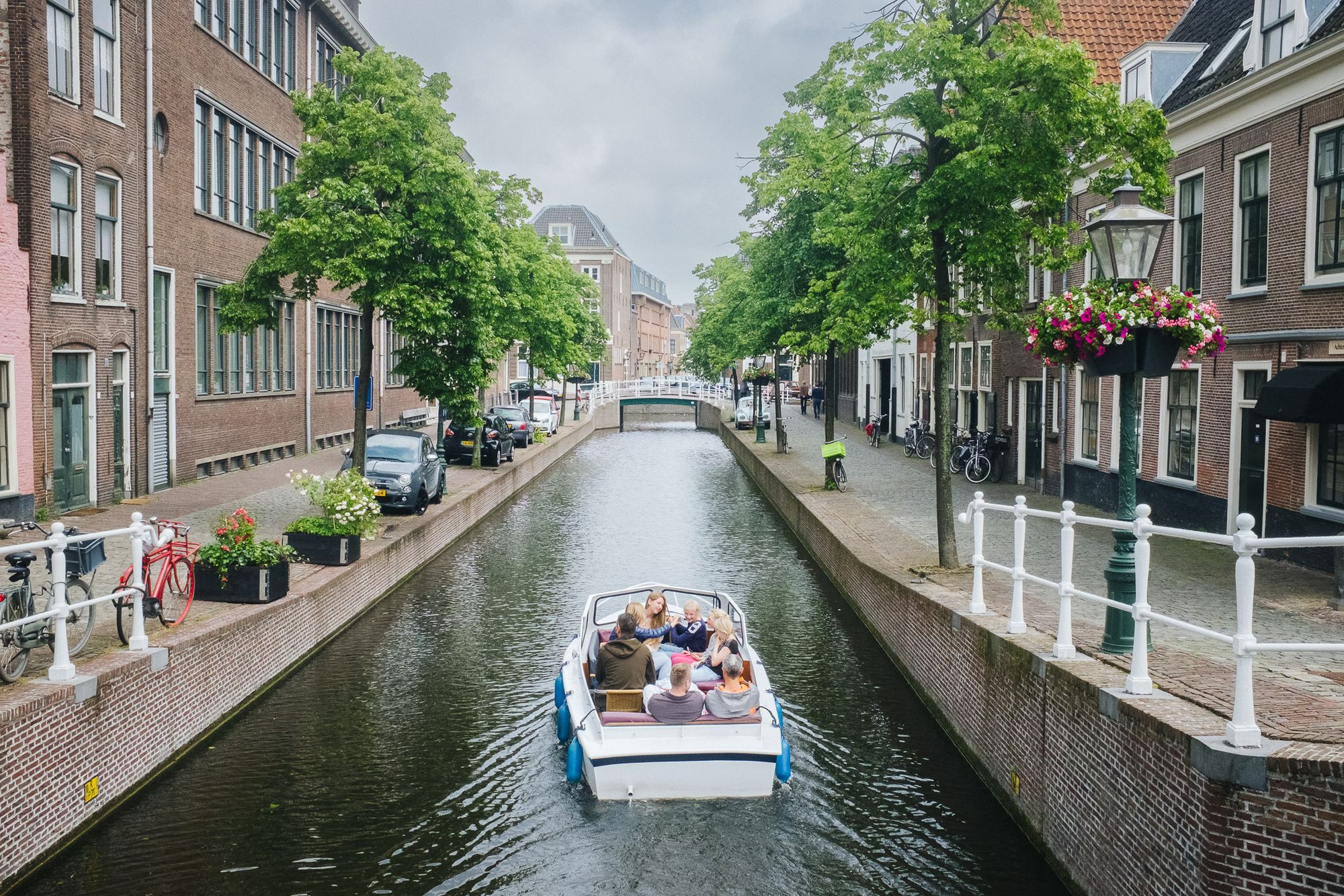 A family boat travels down a canal with trees lining and homes either side.