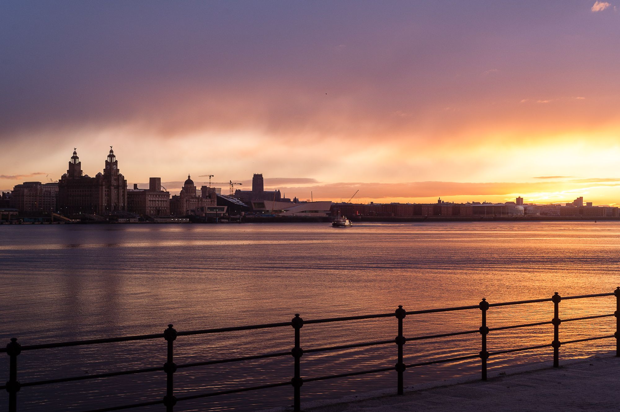 Sunrise over the River Mersey looking towards Liverpool. The Mersey Ferry is coming over and there are purple and yellow colours in the sky.