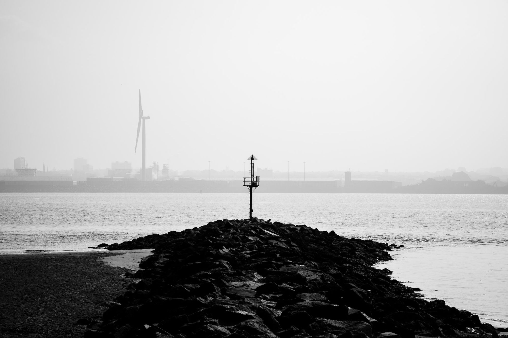 A groyne extending out into the river Mersey on a hazy day.