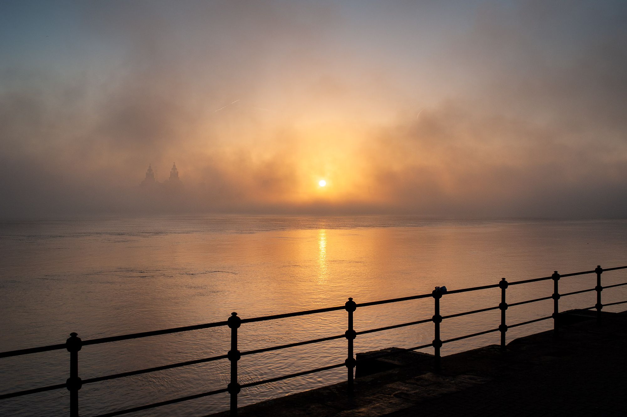 A foggy sunrise over the River Mersey. The Liver Building is barely visible through the fog.