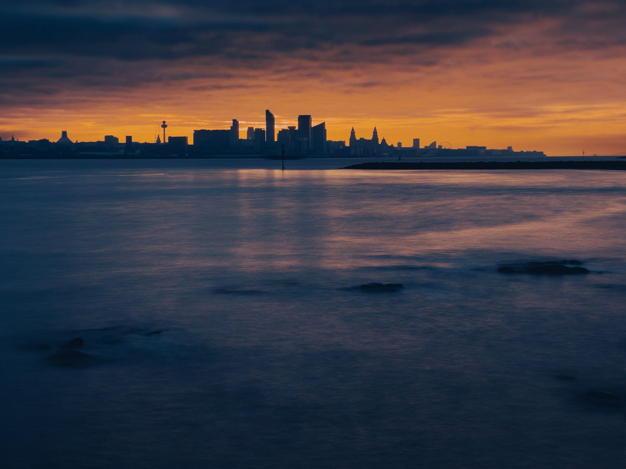Clouds glow with orange colour behind the city of Liverpool at sunrise.