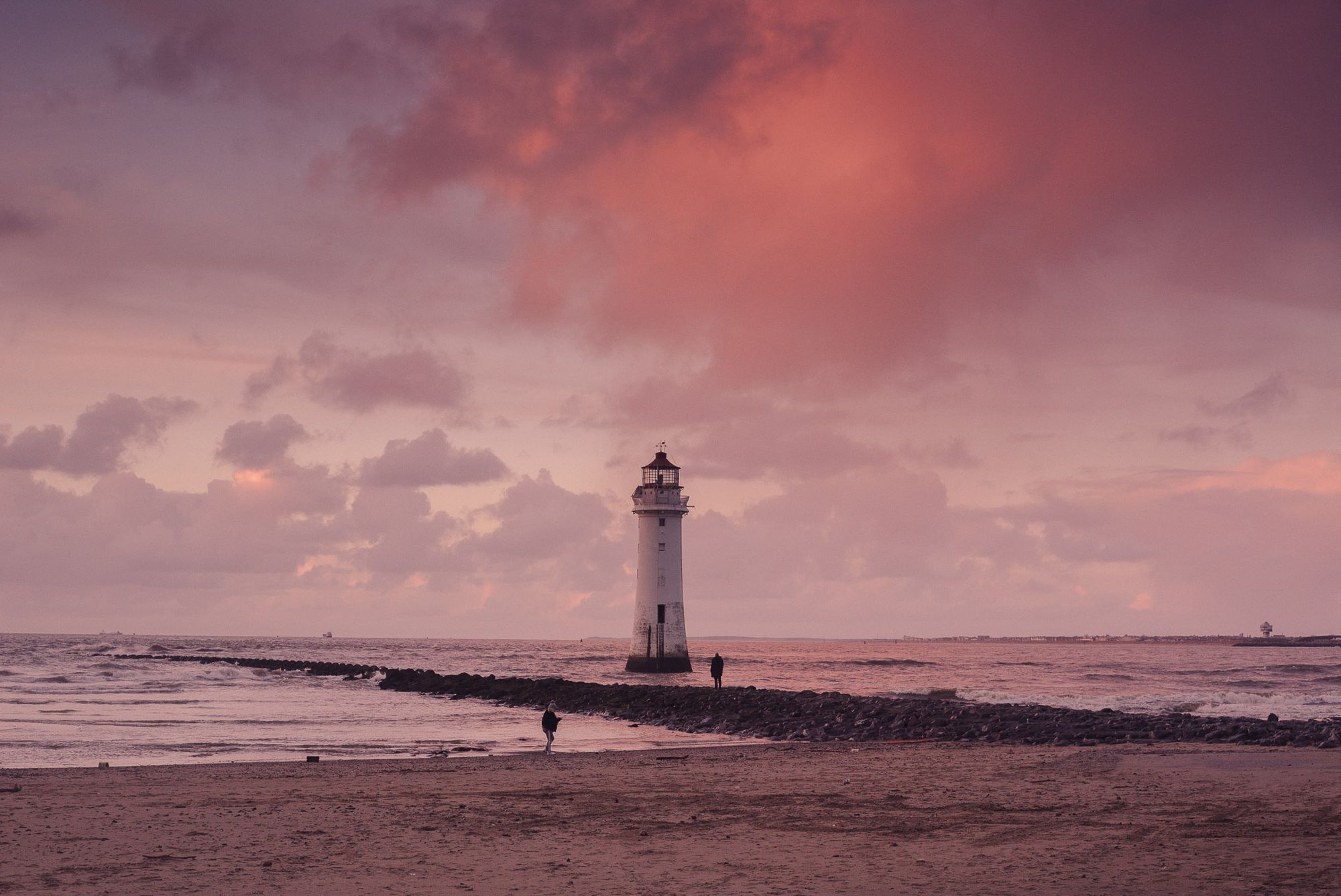 New Brighton lighthouse at sunset. Orange clouds fill the sky and the tide is coming in.