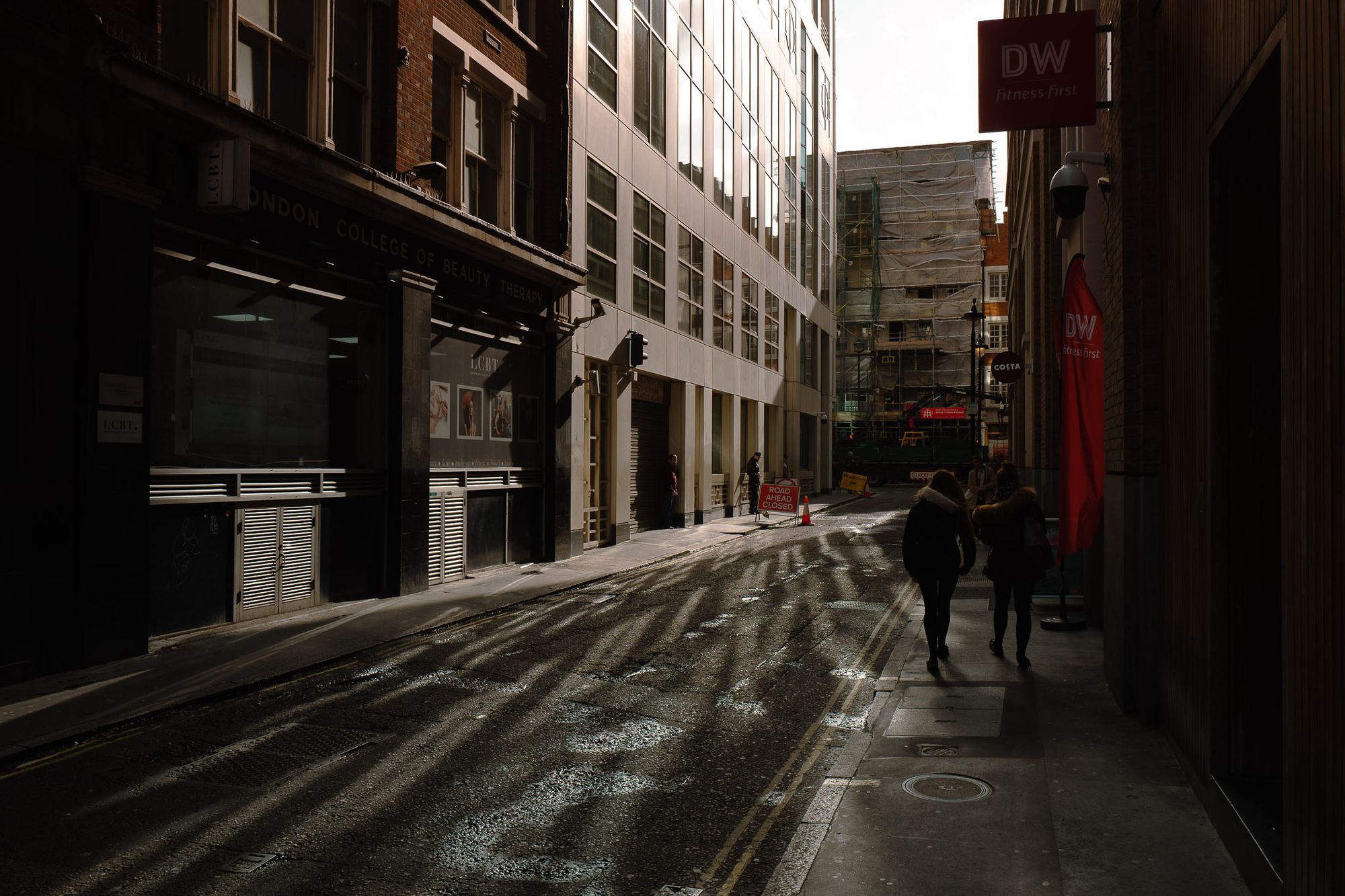 A view down a side-street where the light is bouncing off the windows of a tall building scattering reflections on the street.