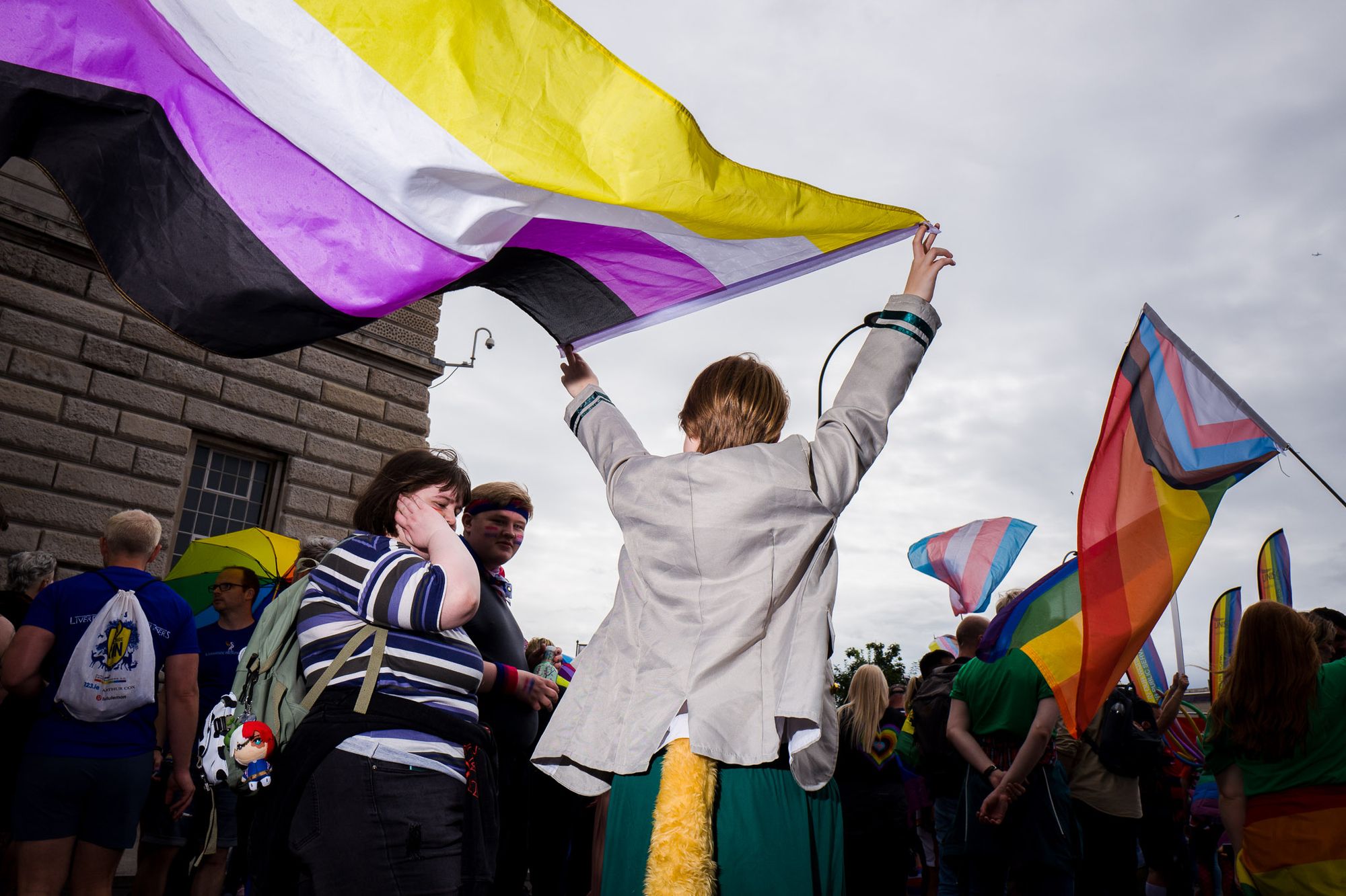 People waving various prides flags. The person closest to camera has a non-binary flag and a yellow tail.