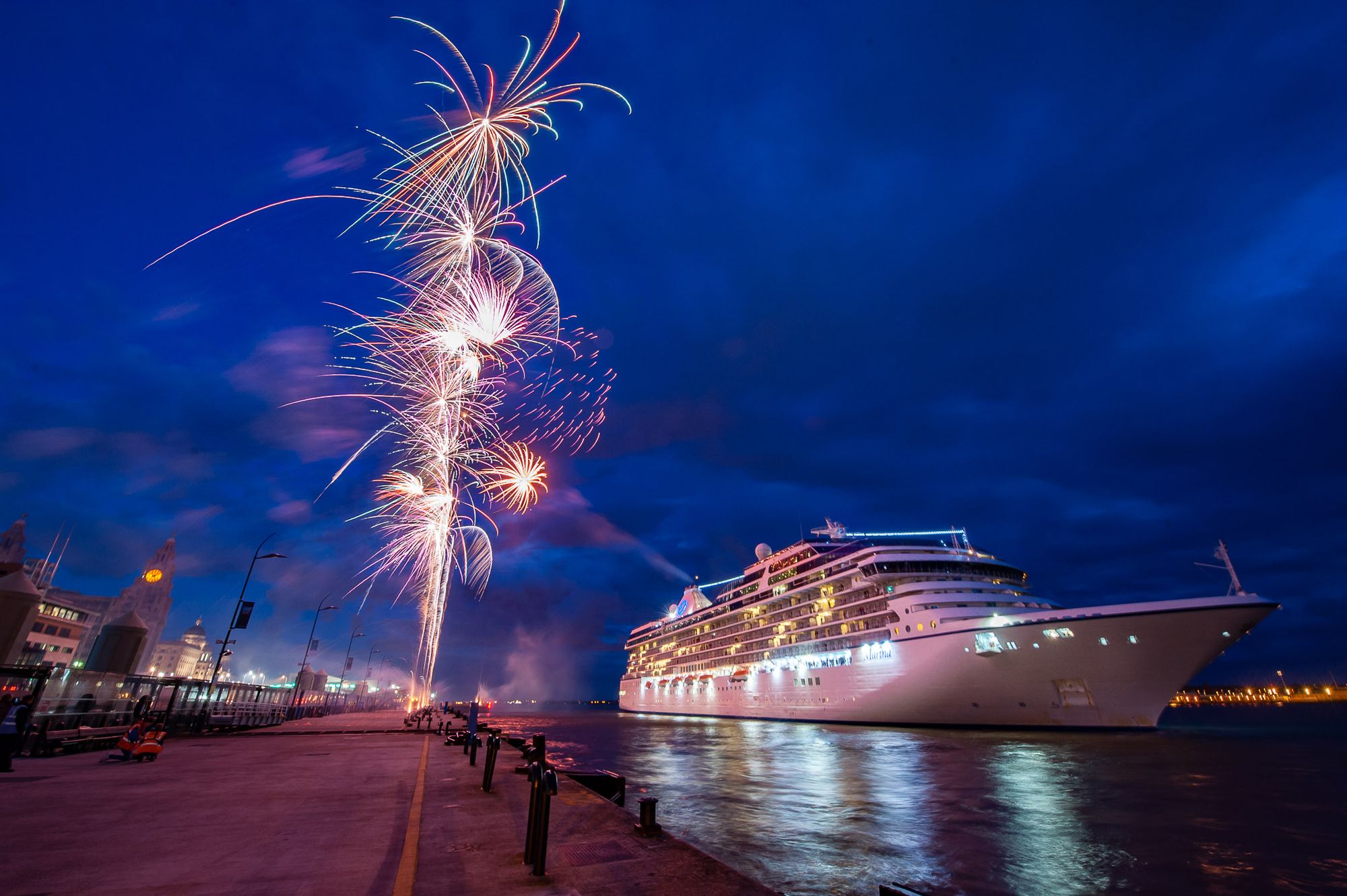 Fireworks fire off from a landing stage while a cruise ship floats in the River Mersey.