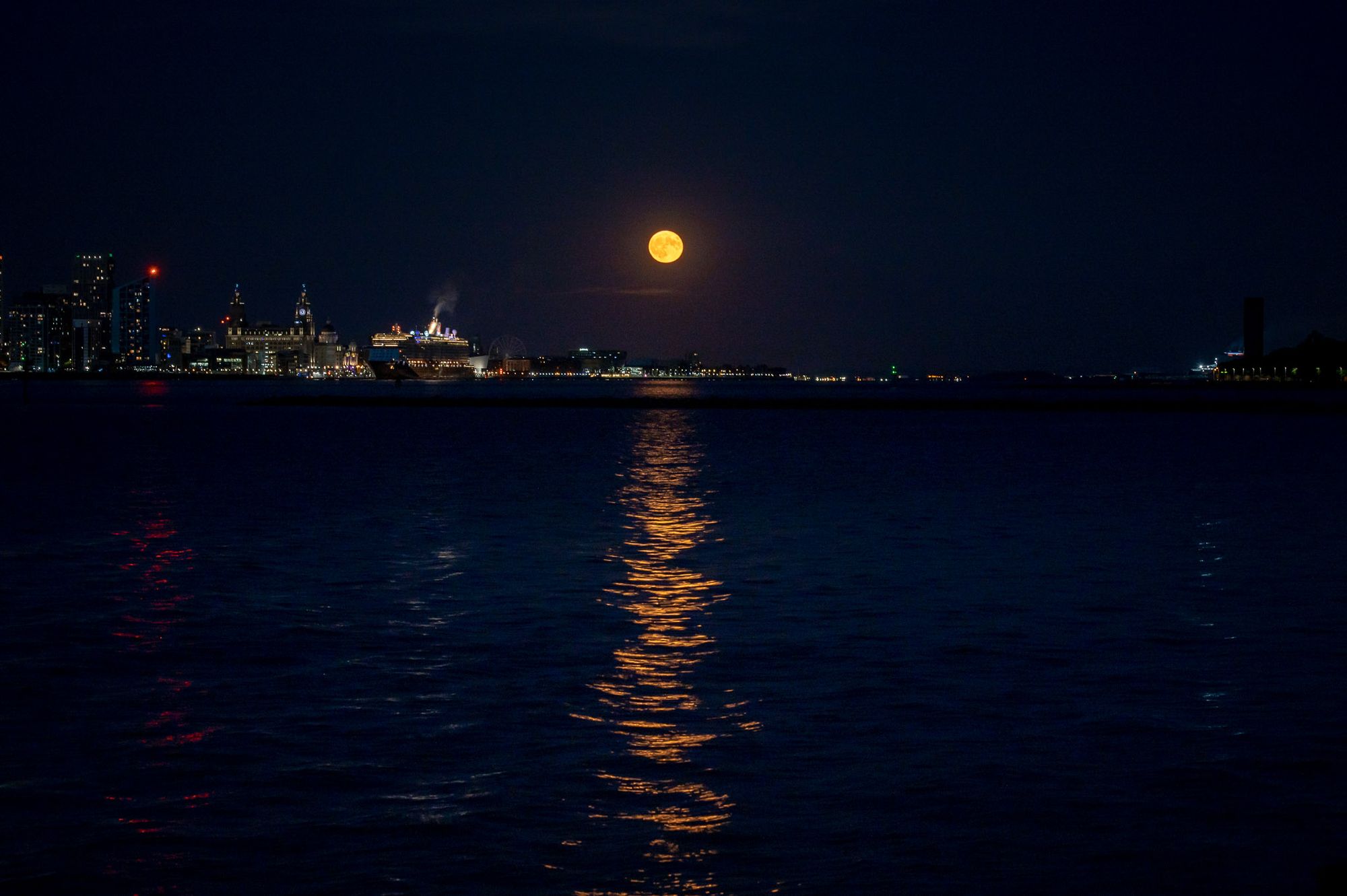 A Strawberry super moon rises to the over the River Mersey with the city of Liverpool to the left.