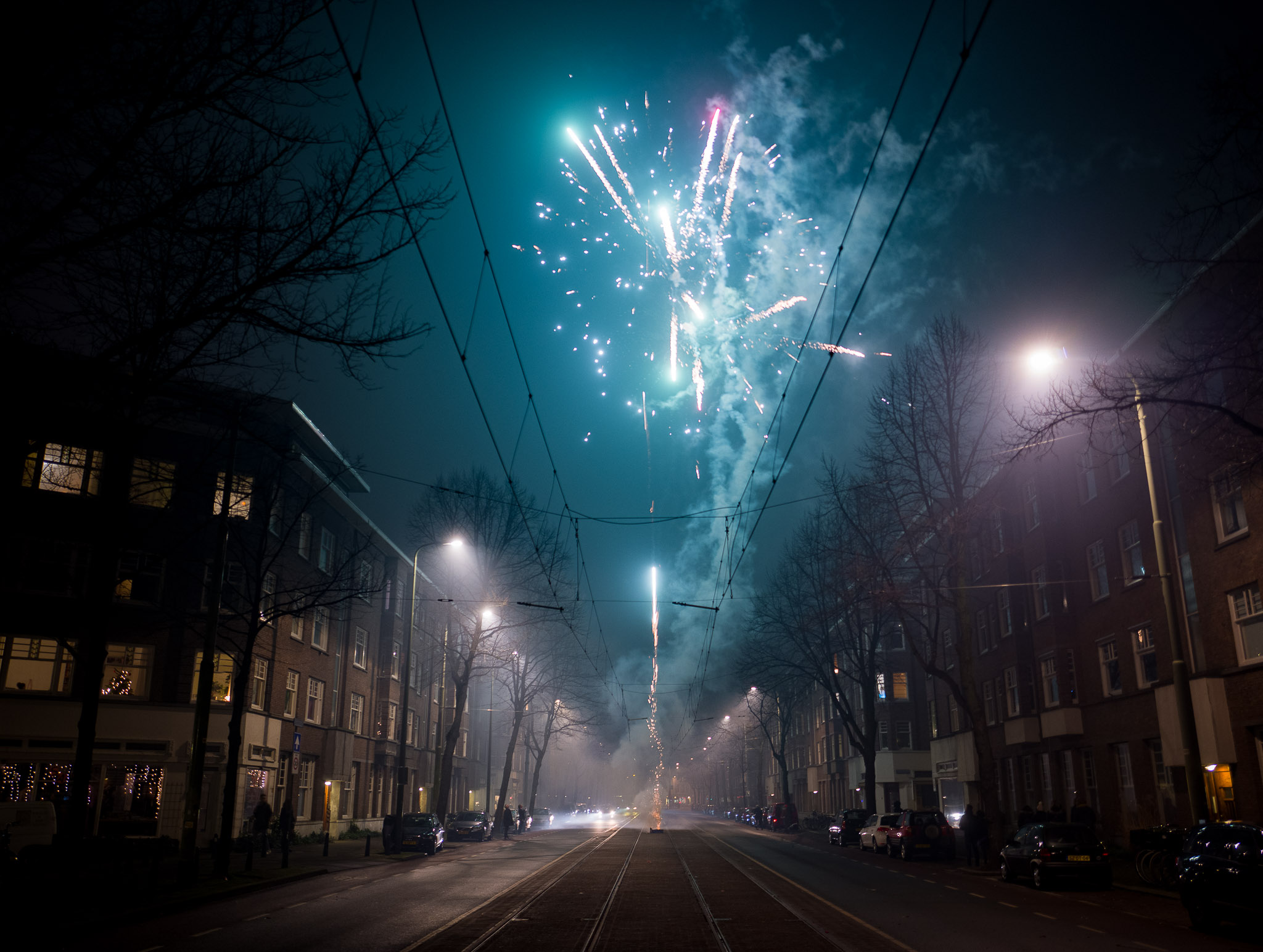 Fireworks launch from the middle of the street high into the sky as traffic passes by. 