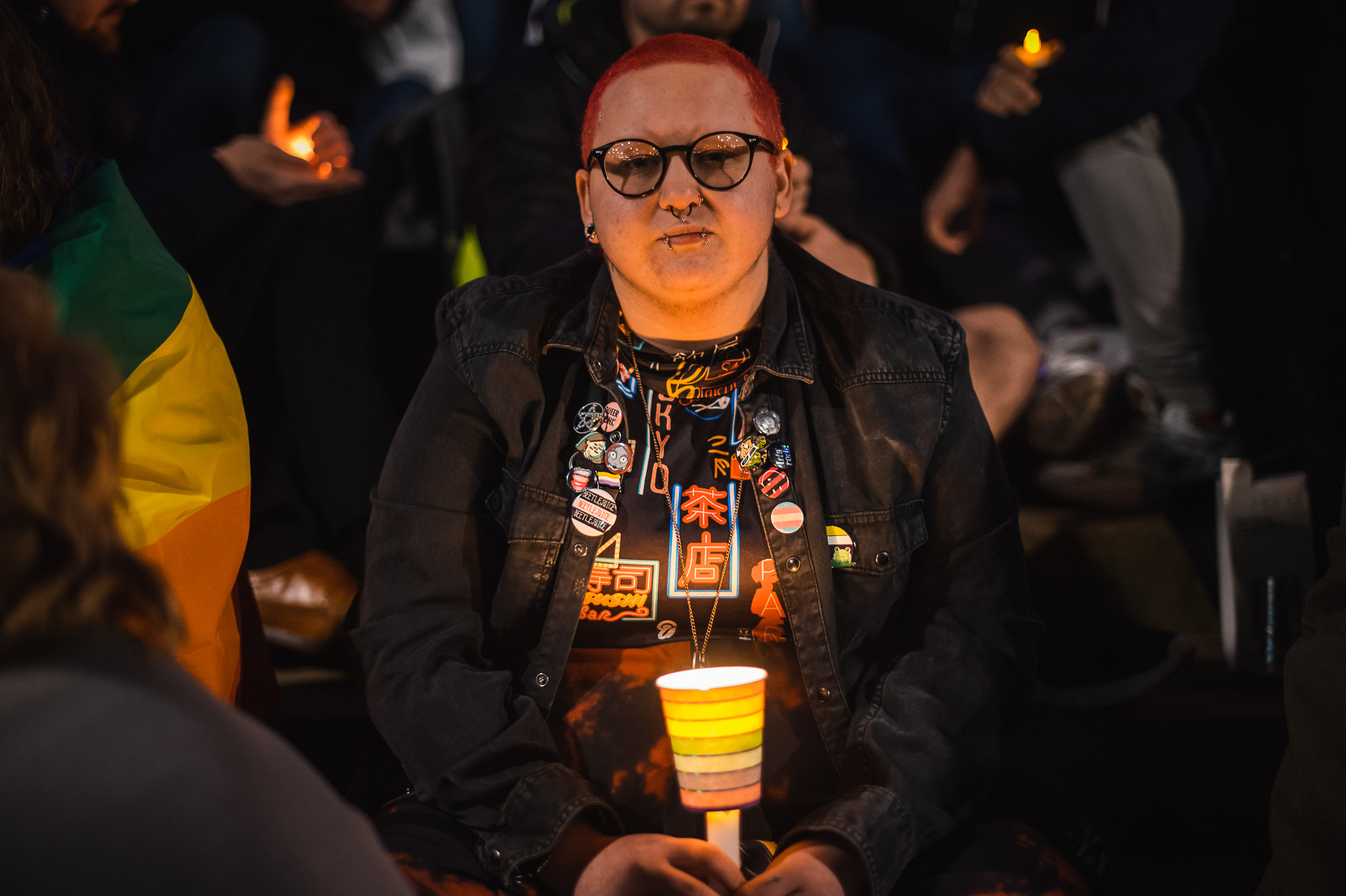 Portrait of a person with short red hair sitting on the steps of St George's Hall. They are holding a candle and looking into the camera.