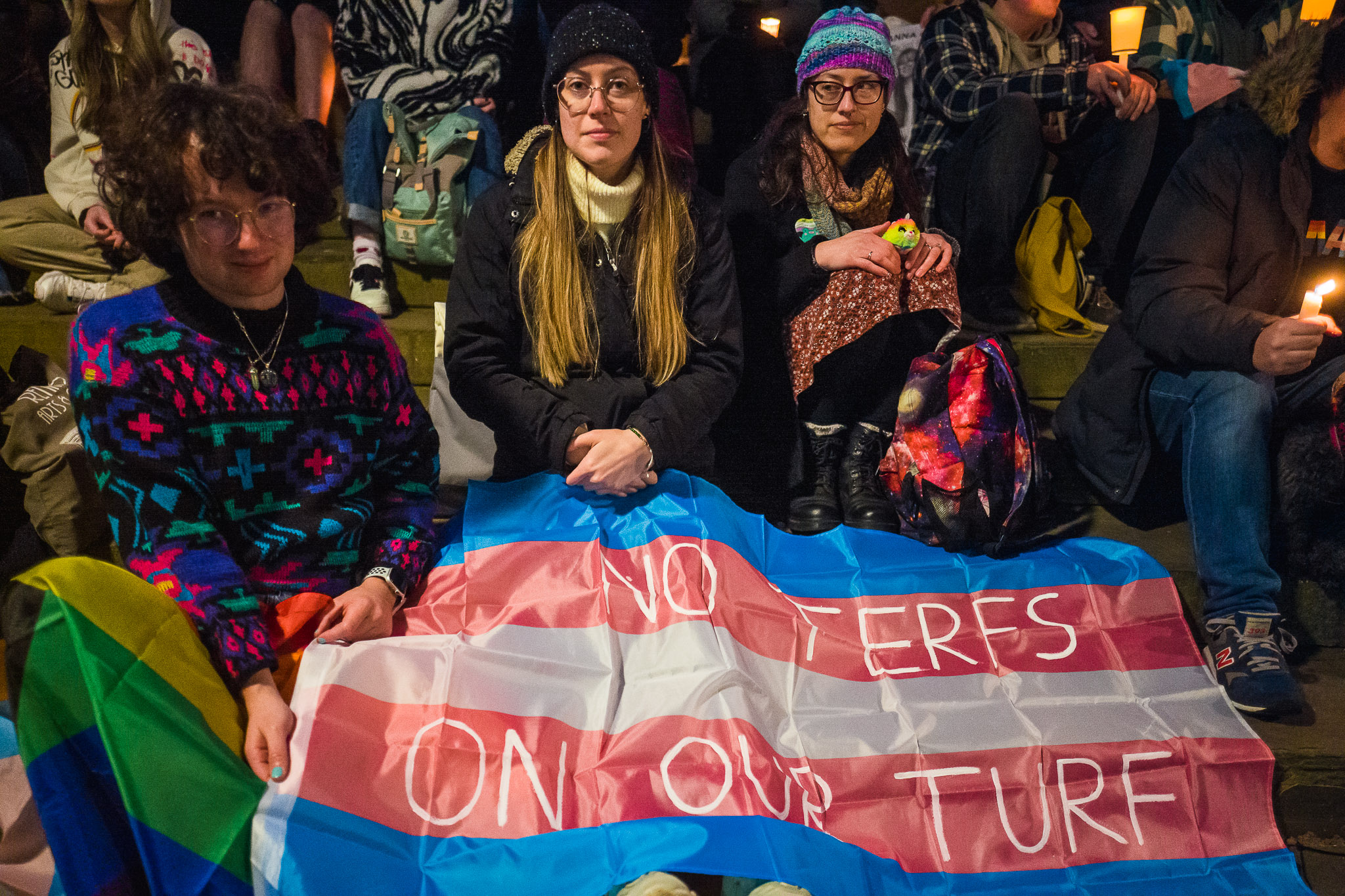 A group of people sitting with a trans flag that has the message "No TERFs on our turf on."