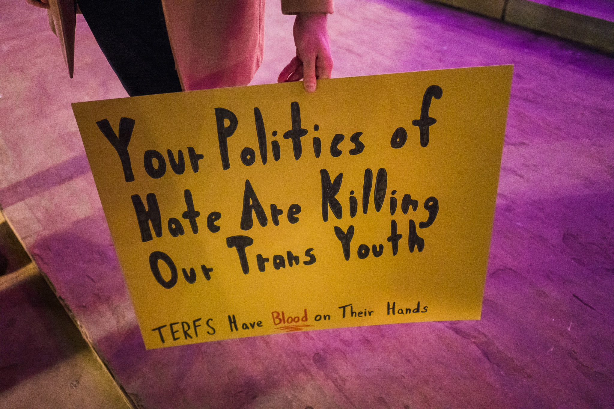 A person holds a sign saying "Your politics of hate are killing our trans youth. TERFs have blood on their hands."