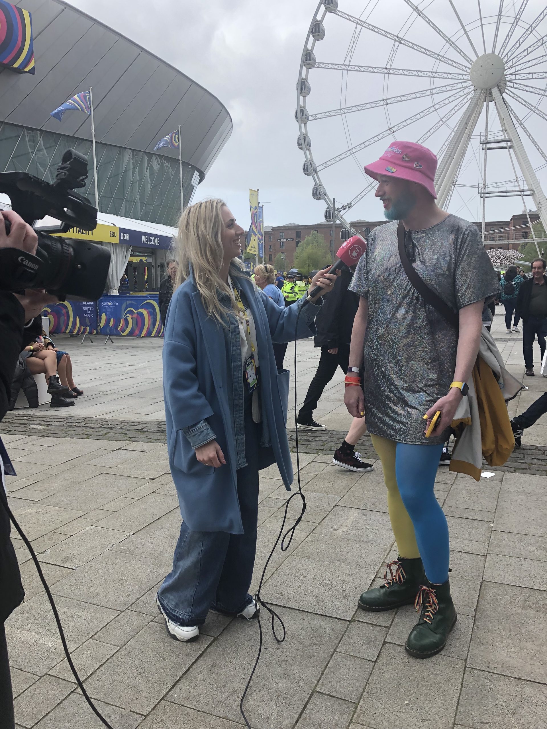 A non-binary person wearing Ukrainian coloured tights and a sparkly t-shirt dress chats to a TV reporter.